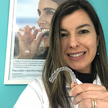 Dra. Laura Coelho segurando uma moldeira do Invisalign enquanto sorri.